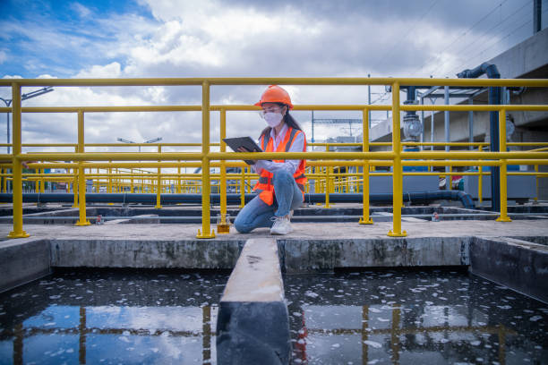 el trabajador toma agua del estanque de tratamiento de aguas residuales para verificar la calidad del agua. después de pasar por el proceso de tratamiento de aguas residuales, ella usa máscara facial para proteger la contaminación en el trabajo. - industry asian ethnicity asia manager fotografías e imágenes de stock