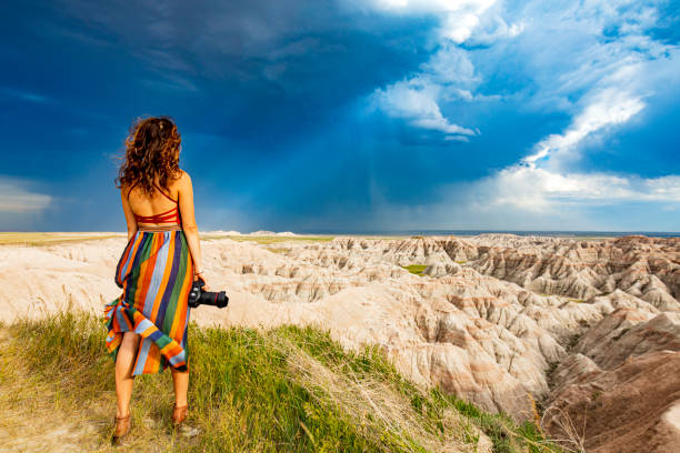 istock Woman holding camera overlooking canyon valley with sun beaming through dark clouds 1329615557