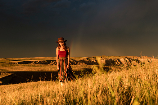 Female model walking through golden valley in front of rainbow after a thunderstorm