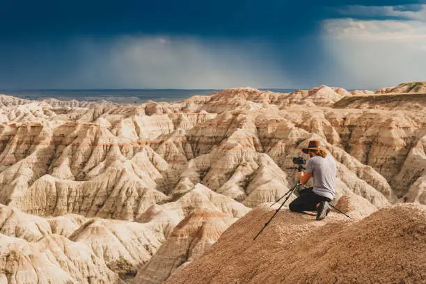 Photo of Man photographing brightly lit canyons in front of a dark stormy sky