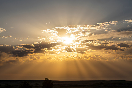 Golden sunrays in the sky peeking through dispersed clouds over vast western plains at sunset