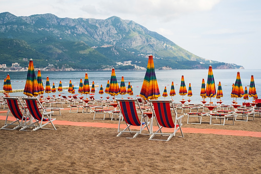 Empty sun loungers without people under rainbow umbrellason the pebble beach by the sea, Montenegro. Empty sun loungers by the sea.