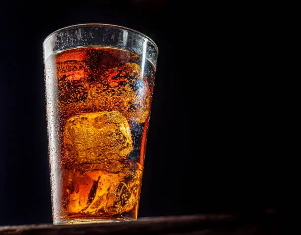 Photo of Chilled glass of cola drink with ice cubes isolated on dark background.