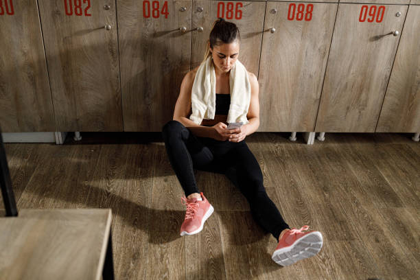 istock Athletic woman using cell phone while resting in dressing room. 1329628145
