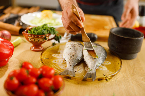 Close up of unrecognizable chef brushing fish before making a healthy meal in the kitchen.