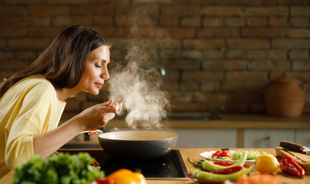 junge frau genießt beim kochen mahlzeit in der küche. - tasting stock-fotos und bilder