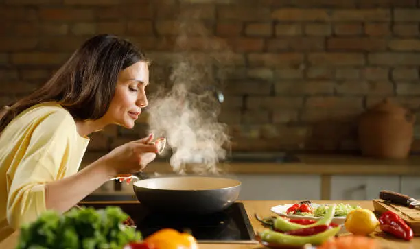 Photo of Young woman enjoying while cooking meal in the kitchen.