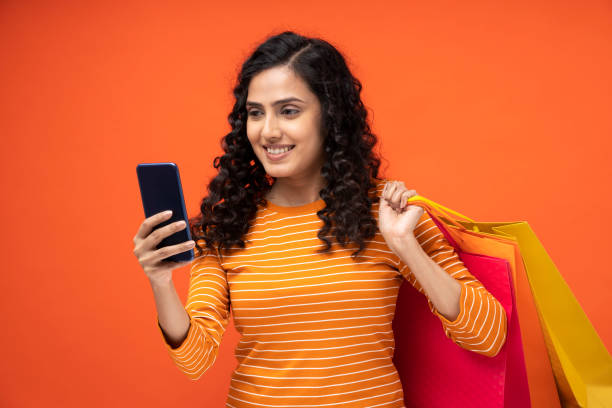 tiro de uma jovem mulheres carregando saco de compras em pé isolado sobre fundo laranja - fashion model asian ethnicity curly hair enjoyment - fotografias e filmes do acervo