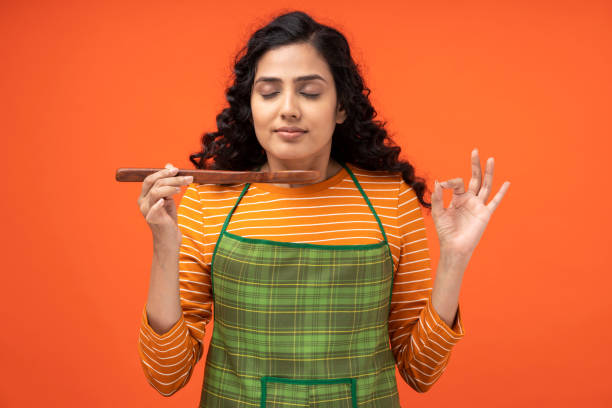 Portrait of young women chef tasting the vegetable soup holding wooden spoon standing isolated over orange background India, young women, Cooking, One Woman Only, Indian Ethnicity high quality kitchen equipment stock pictures, royalty-free photos & images