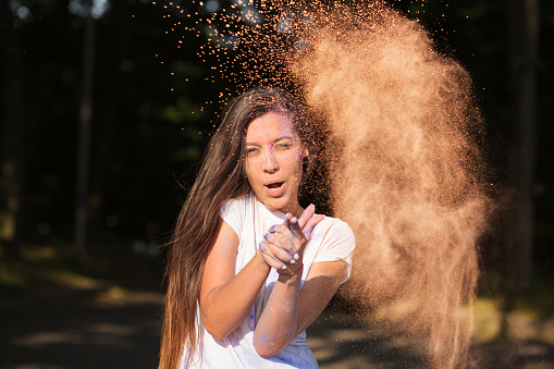 Emotional young asian woman having fun with orange dry paint on Holi festival