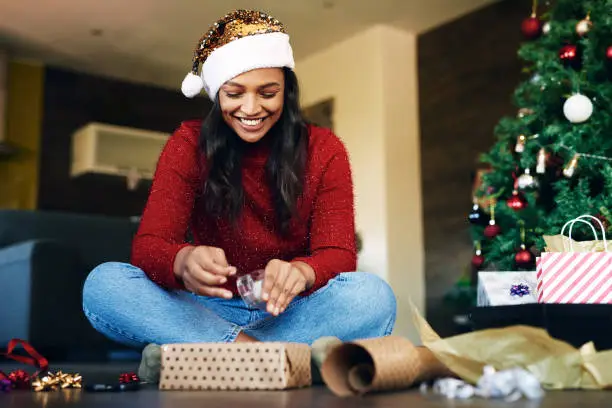 Photo of Shot of a young woman wrapping Christmas gifts at home