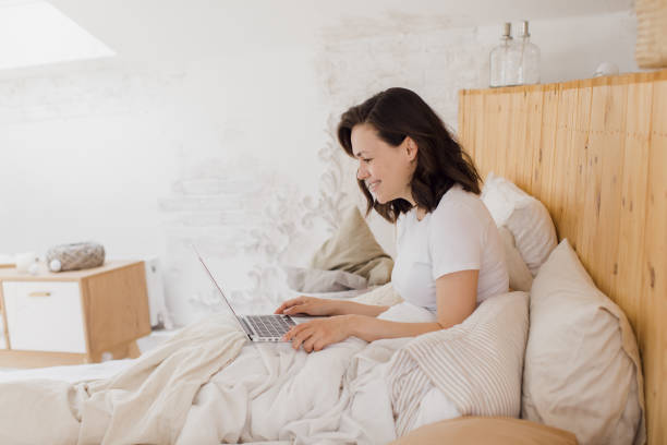 istock Happy beautiful woman working on a laptop while sitting on a bed in a bright modern house. 1329641306