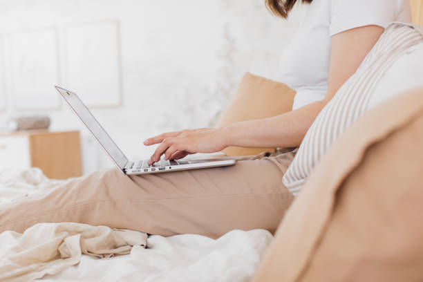 istock Happy beautiful woman working on a laptop while sitting on a bed in a bright modern house. 1329641410
