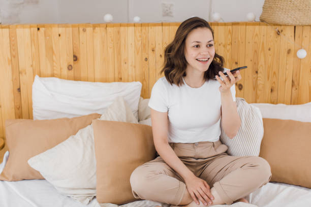istock Smiling young Caucasian woman record digital audio message on smartphone in modern flat 1329642996