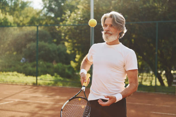 czas szkolenia. starszy nowoczesny stylowy mężczyzna z rakietą na zewnątrz na korcie tenisowym w ciągu dnia - tennis men vitality joy zdjęcia i obrazy z banku zdjęć
