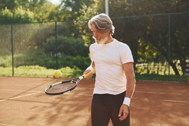 czas szkolenia. starszy nowoczesny stylowy mężczyzna z rakietą na zewnątrz na korcie tenisowym w ciągu dnia - tennis men vitality joy zdjęcia i obrazy z banku zdjęć