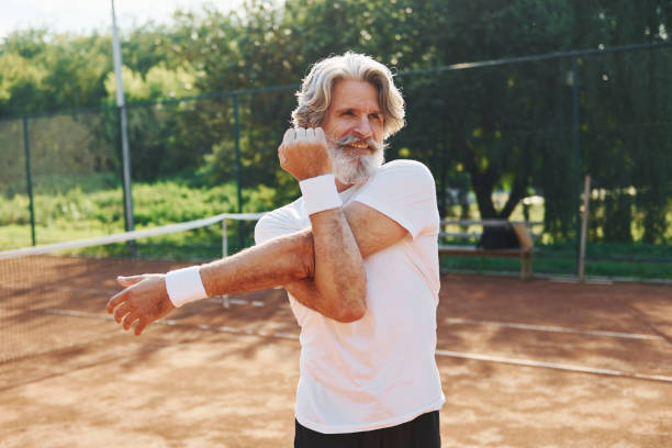 wykonywanie ćwiczeń rozgrzewkowych. starszy nowoczesny stylowy człowiek na świeżym powietrzu na boisku sportowym w ciągu dnia - tennis men vitality joy zdjęcia i obrazy z banku zdjęć