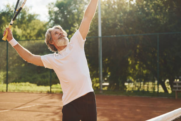 gra. starszy nowoczesny stylowy mężczyzna z rakietą na zewnątrz na korcie tenisowym w ciągu dnia - tennis men vitality joy zdjęcia i obrazy z banku zdjęć