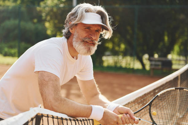starszy nowoczesny stylowy mężczyzna z rakietą na zewnątrz na korcie tenisowym w ciągu dnia - tennis men vitality joy zdjęcia i obrazy z banku zdjęć