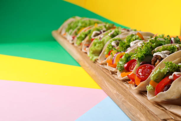 Many delicious vegetarian tacos served on color table, closeup. Space for text