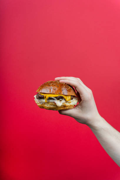 istock human hand holding tasty hamburger cheeseburger burger isolated on red background 1329649389