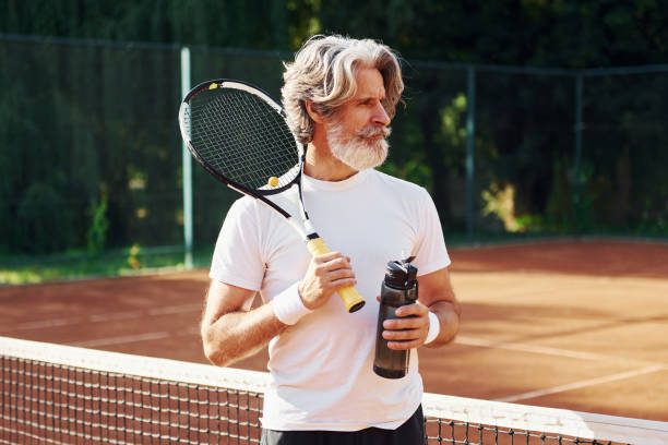 물 병을 들고. 낮에 테니스 코트에서 라켓 아웃도어를 갖춘 시니어 모던 세련 된 남자 - men gray hair vitality healthy lifestyle 뉴스 사진 이미지