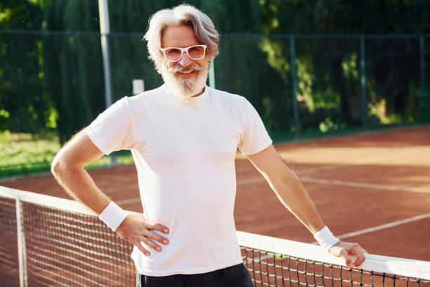 pozowanie do kamery. w okularach przeciwsłonecznych. starszy nowoczesny stylowy człowiek na świeżym powietrzu na boisku sportowym w ciągu dnia - tennis men vitality joy zdjęcia i obrazy z banku zdjęć