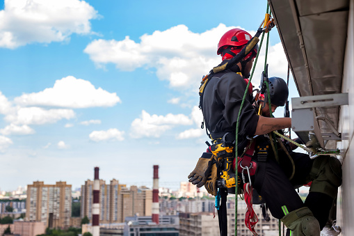 Industrial mountaineering worker hangs over residential building while installing and repairing equipment. Rope access laborer hangs on wall of house. Concept of high-rise urban works. Copy space