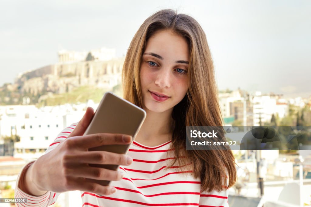 Beautiful young woman makes selfie on the background of a cityscape Beautiful young woman makes selfie on the background against Parthenon temple on Acropolis in Athens, Greece 14-15 Years Stock Photo