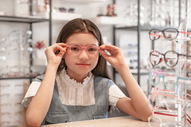 Portrait of smiling girl customer selecting spectacles in optical store stock photo