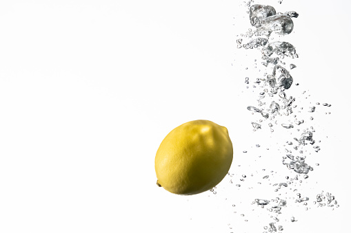 Yellow lemon dropped into water on white