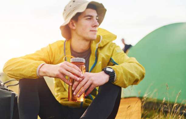 istock Man in hat sitting outdoors near green tent and taking a rest 1329655356