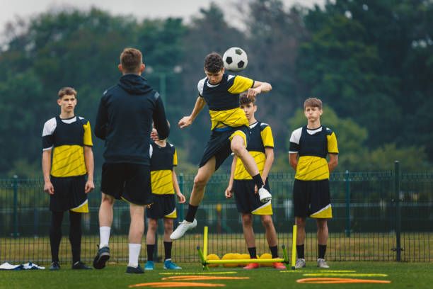 teenage football players training headshots  young player jumping high and head ball. coach coaching junior youth football club. soccer training equipment on grass field - soccer ball youth soccer event soccer imagens e fotografias de stock