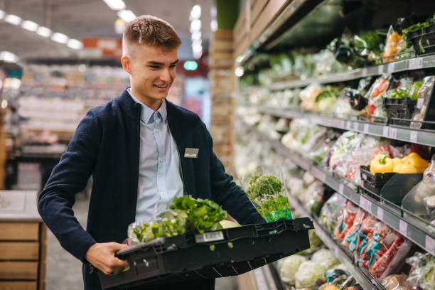Shop assistant restocking the produce section shelves Shop assistant in supermarket re-stocking fresh vegetables in shelves of produce section. supermarket stock pictures, royalty-free photos & images
