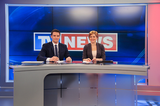 Man and woman sitting at news desk in a tv recording studio.