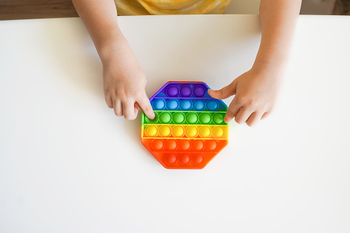 Pop it fidget in kid's hands. Colorful toy push pop it. Top view of antistress sensory fidget.