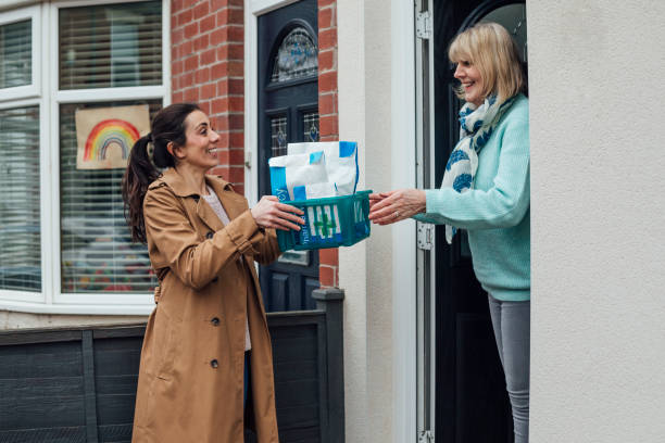 Contactless Prescription Delivery Medium shot of a woman answering her front door to a pharmacist wearing a protective face mask who is delivering a prescription. The woman accepts the package and they say goodbye before she closes the door. They are in the North east of England. home delivery photos stock pictures, royalty-free photos & images