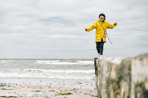 little girl in yellow raincoat balancing on groyne at beach of baltic sea