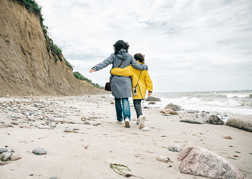 little girl in yellow raincoat walking embraced with mother on stone beach