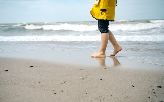 side view on little girl in yellow raincoat walking barefoot at beach of the baltic sea