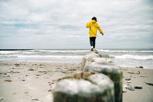 rear view on little girl in yellow raincoat balancing on groyne at beach of baltic sea