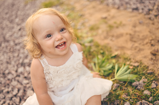 Two-Year-Old Toddler Girl Sitting on the Floor in a Cream-Colored Linen Dress & a Bow at Home During COVID-19