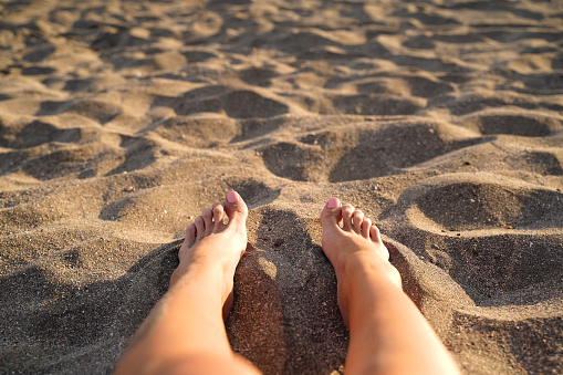 Beautiful female feet on the sand of the beach. Relaxation and enjoyment during your seaside holiday.