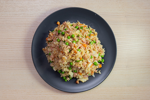 A plate of fried rice with bacon bits and peas.