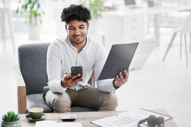 istock Shot of a young businessman using a cellphone while going through paperwork in an office 1329681464