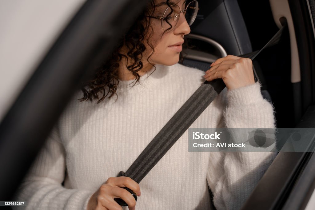 European girl buckles down seat belt in car European girl buckles down seat belt in car. Concentrated young curly woman wearing glasses. Concept of driving car Seat Belt Stock Photo