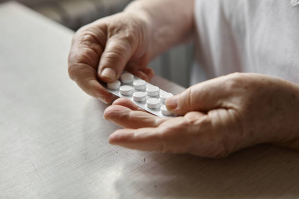 istock Sad old woman taking pills, health problems in old age, expensive medications. An elderly woman's hands unpacking several pills for taking medication. Grandma takes tablet and drinks a glass of water 1329683462