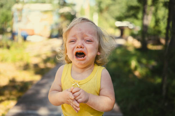 Close up portrait of little funny cute blonde girl child toddler in yellow bodysuit crying outside at summer. Childish tantrum. Healthy childhood concept. stock photo