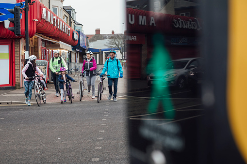 Multi generation mixed race family on a bike ride near the coast. They are crossing the road with their bikes along a seaside street in the North east of England.