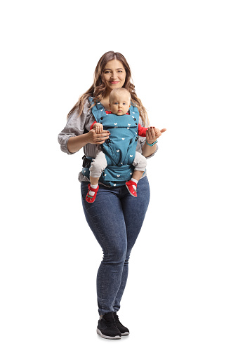 Full length portrait of a mother with a baby in a carrier smiling at camera isolated on white background